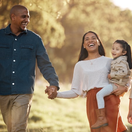 A family of three walking in a park at sunset